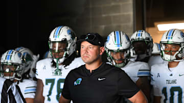 Tulane Green Wave college football coach Jon Sumrall walks out tunnel with his players behind him.